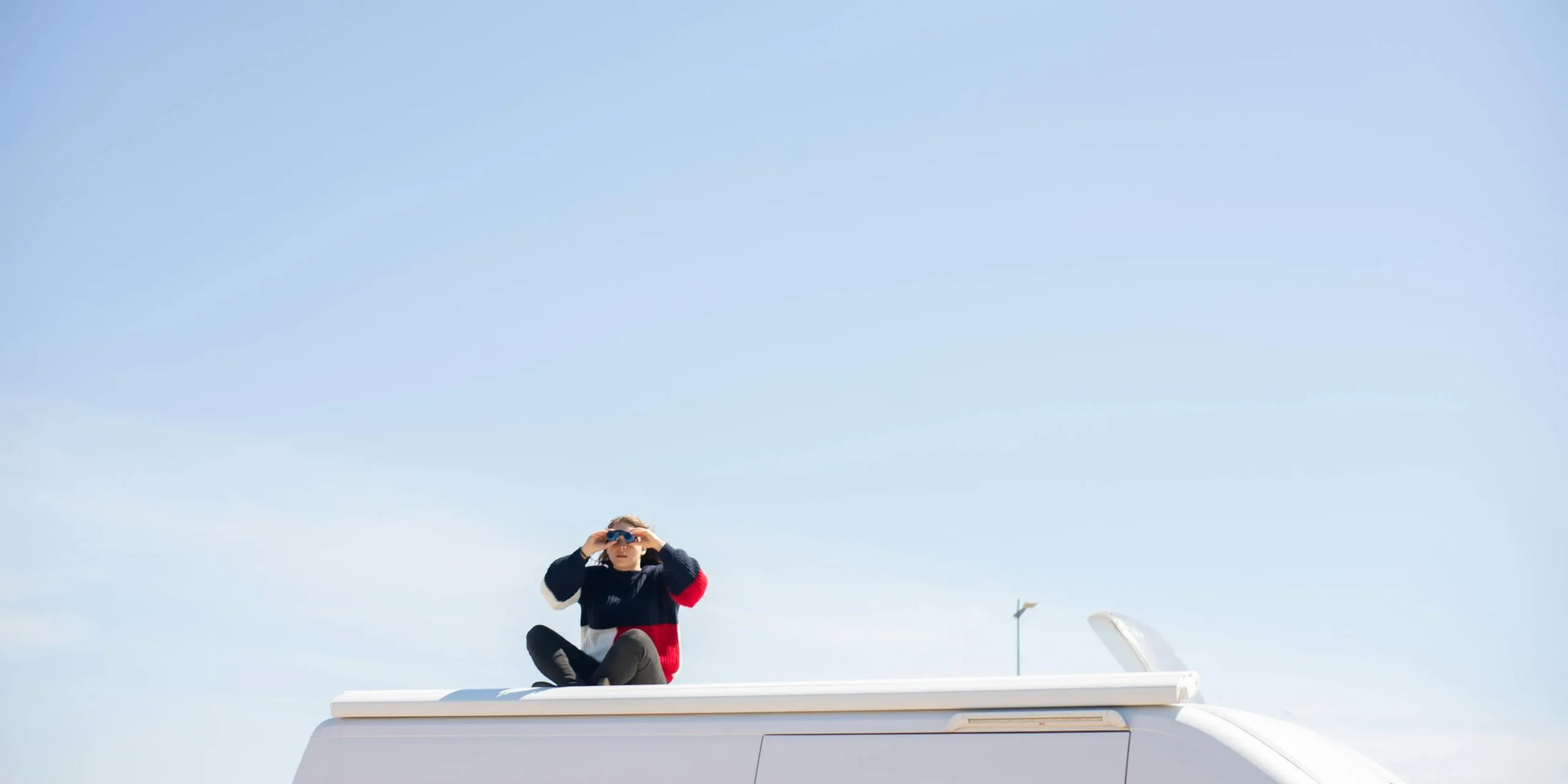 Photo of a woman sitting on top of a van with binoculars