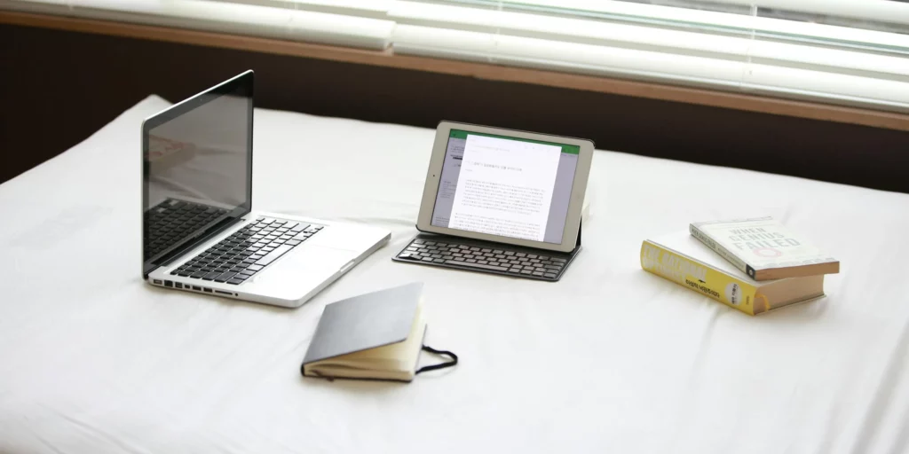 Photo of a laptop and ipad with books and a notebook
