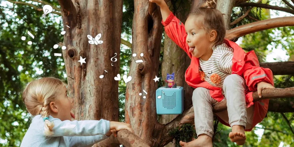 Two little girls playing in a tree with a Tonies box